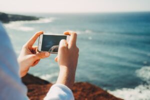 海辺でiPhoneで写真を撮っている白い服の人